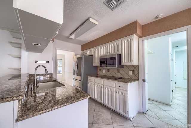 kitchen with visible vents, dark stone countertops, stainless steel appliances, white cabinetry, and a sink