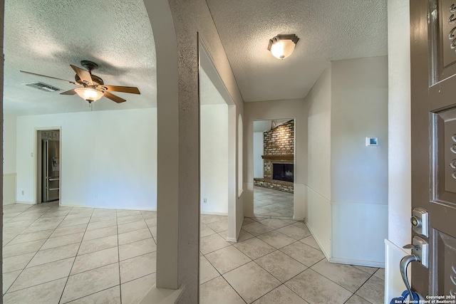 interior space with a brick fireplace, light tile patterned flooring, visible vents, and ceiling fan