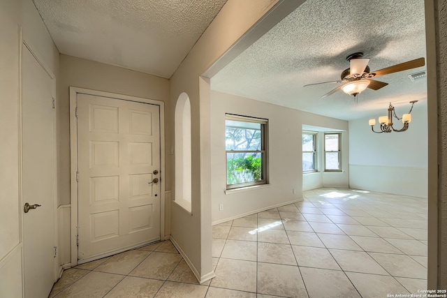 foyer entrance with visible vents, ceiling fan with notable chandelier, a textured ceiling, light tile patterned floors, and baseboards