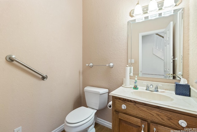 bathroom featuring vanity, toilet, a textured wall, and baseboards