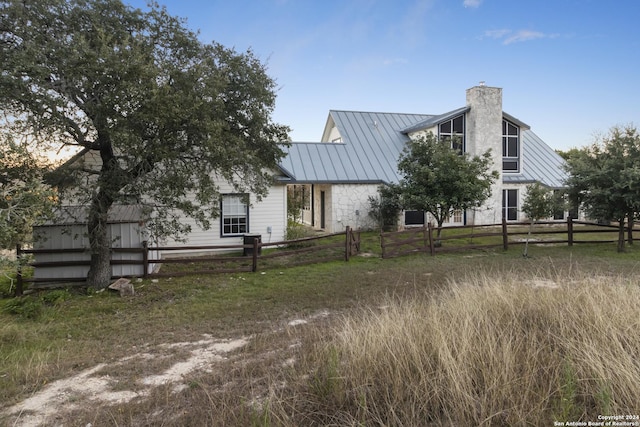 view of front of property with fence, a chimney, metal roof, stone siding, and a standing seam roof