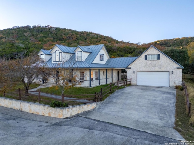 view of front facade featuring driveway, a standing seam roof, stone siding, fence, and metal roof