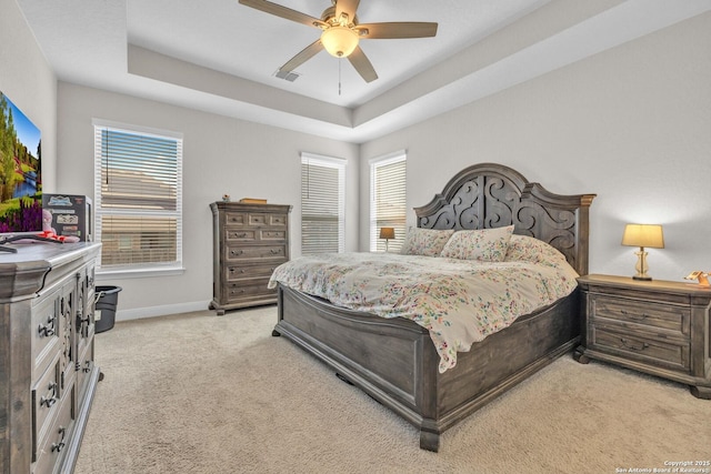 bedroom with light colored carpet, a tray ceiling, and multiple windows