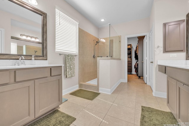 bathroom with tile patterned flooring, a walk in shower, a walk in closet, two vanities, and a sink