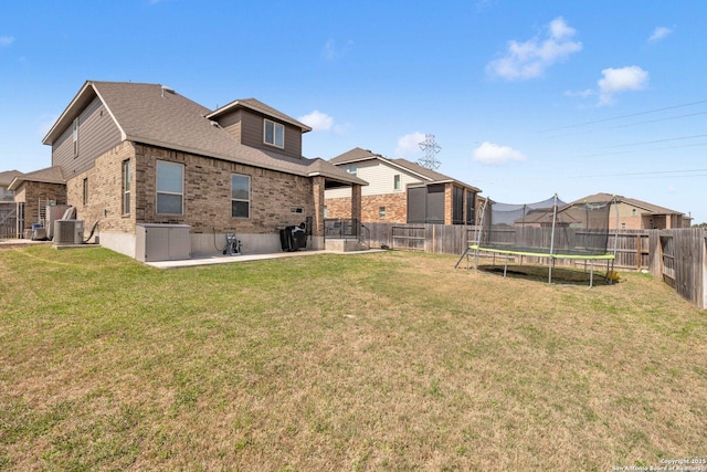 rear view of house with cooling unit, a yard, a fenced backyard, a trampoline, and brick siding