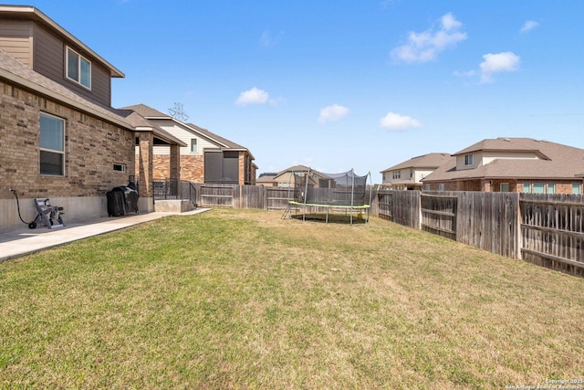 view of yard featuring a trampoline, a fenced backyard, and a residential view