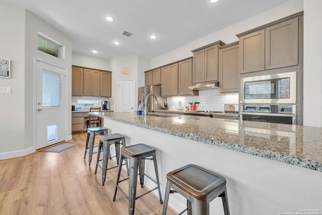 kitchen with under cabinet range hood, decorative backsplash, appliances with stainless steel finishes, a kitchen breakfast bar, and a sink