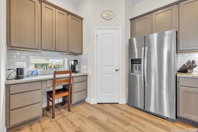 kitchen with light stone counters, decorative backsplash, light wood-style flooring, and stainless steel fridge with ice dispenser