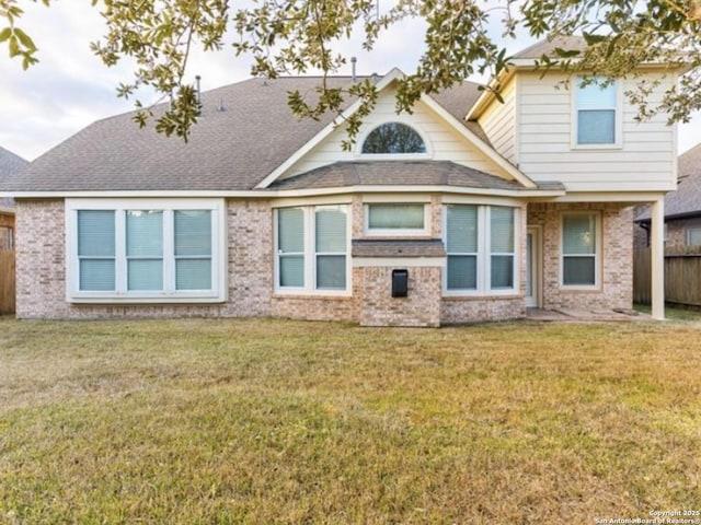 rear view of property featuring a lawn, roof with shingles, brick siding, and fence