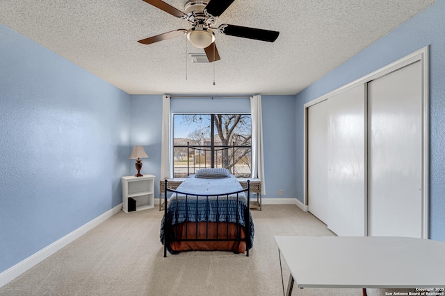 bedroom with a closet, light colored carpet, a textured ceiling, and baseboards