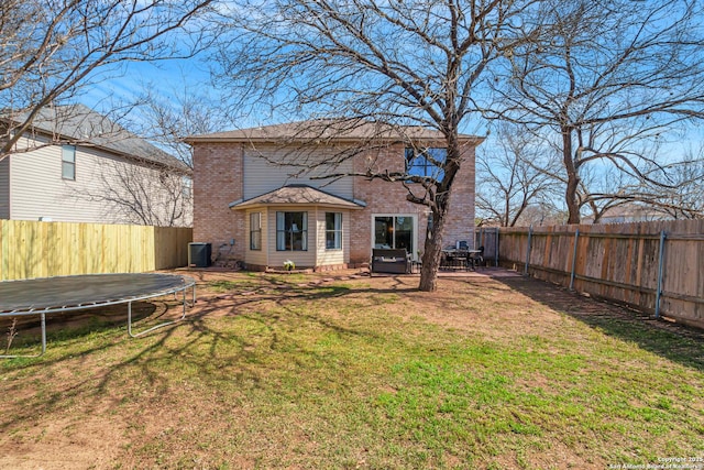 back of house featuring a fenced backyard, central AC, a trampoline, a lawn, and brick siding