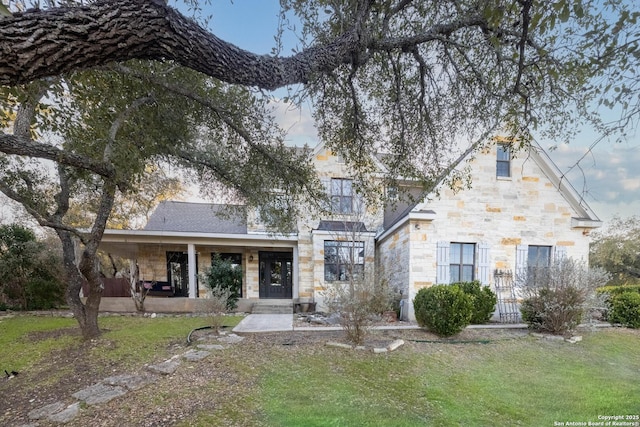 view of front facade featuring a front yard, covered porch, and stone siding