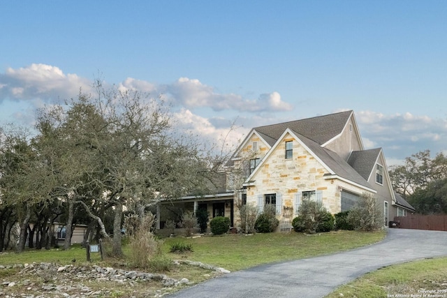 view of front of house featuring a front yard, stone siding, and aphalt driveway