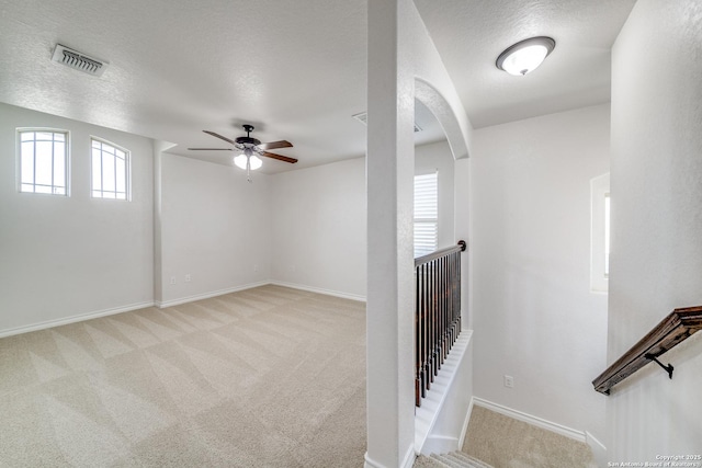 carpeted empty room with arched walkways, visible vents, a textured ceiling, and baseboards