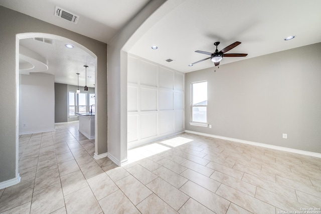 spare room with light tile patterned floors, baseboards, visible vents, arched walkways, and ceiling fan