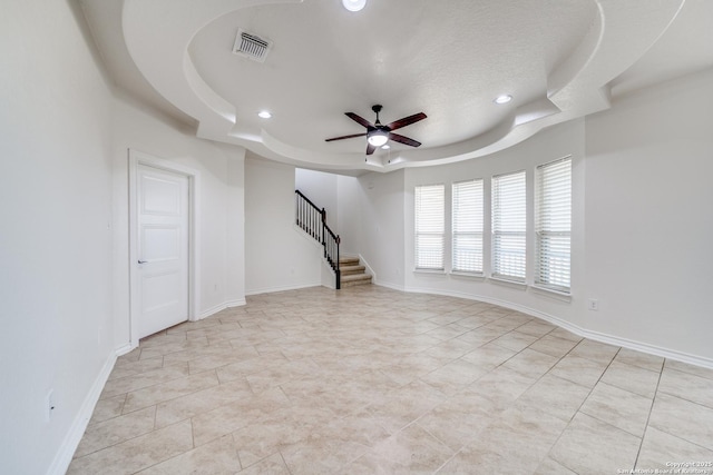 spare room featuring a tray ceiling, stairway, baseboards, and visible vents