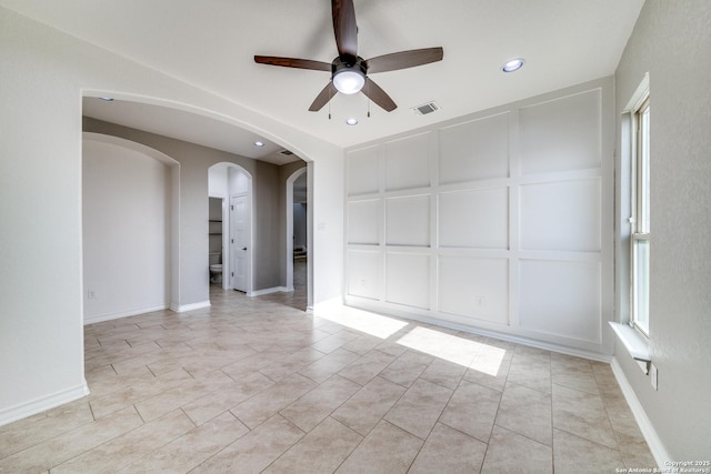 empty room with light tile patterned floors, visible vents, arched walkways, ceiling fan, and a decorative wall