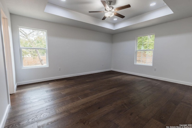 empty room featuring a raised ceiling, baseboards, and dark wood-style flooring