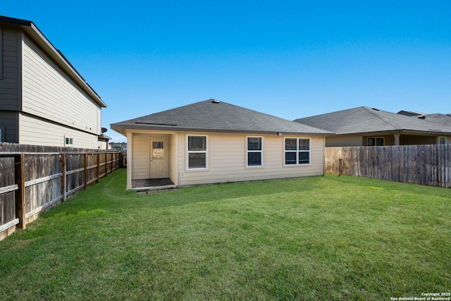 rear view of house with a fenced backyard, a yard, and roof with shingles