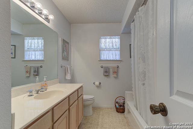 bathroom featuring baseboards, toilet, shower / tub combo with curtain, vanity, and a textured ceiling