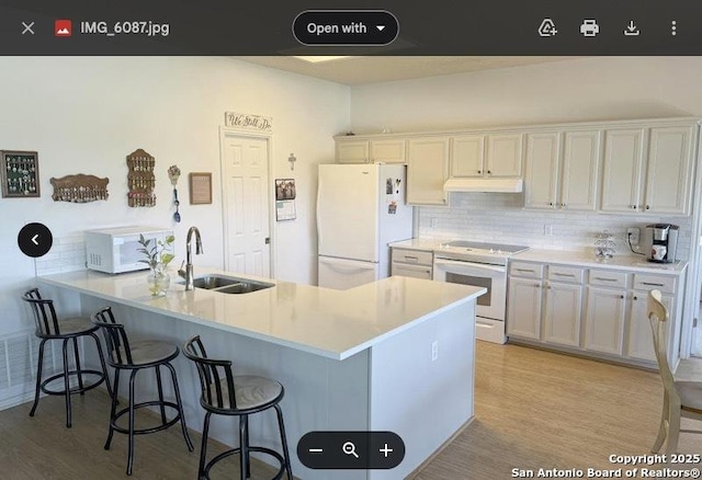 kitchen featuring under cabinet range hood, a kitchen bar, white appliances, and a sink