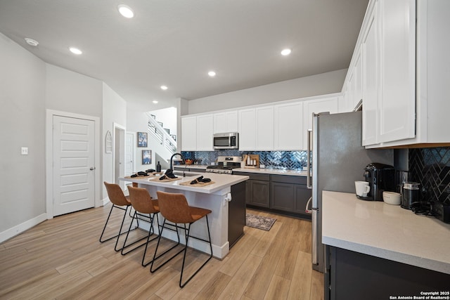 kitchen featuring a kitchen bar, light wood-style flooring, white cabinets, and appliances with stainless steel finishes