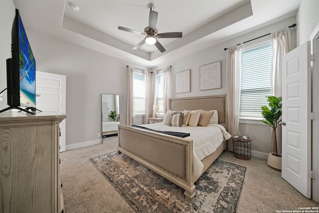 bedroom featuring light colored carpet, a tray ceiling, a ceiling fan, and baseboards