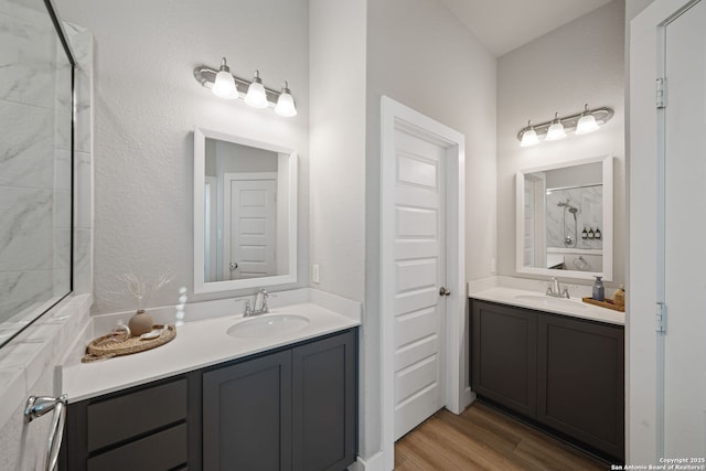 bathroom with walk in shower, two vanities, wood finished floors, and a sink