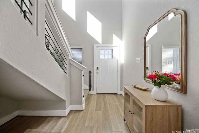 entrance foyer featuring stairs, a high ceiling, light wood-style flooring, and baseboards