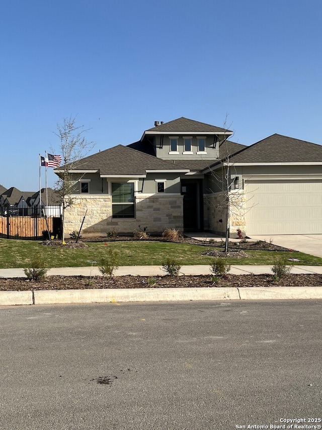 prairie-style house with stone siding, an attached garage, a front yard, and fence