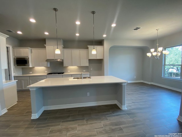 kitchen with visible vents, a large island, a sink, stainless steel microwave, and black stovetop