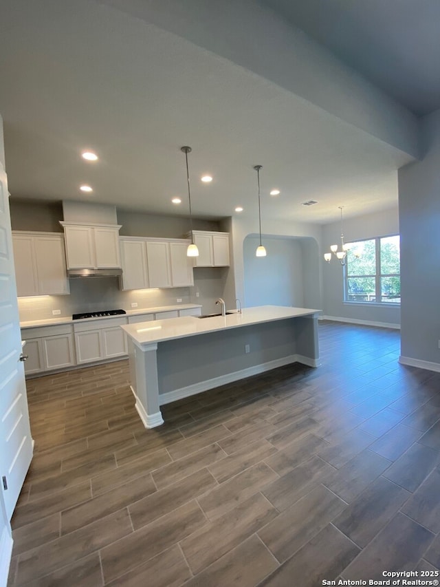 kitchen with wood tiled floor, light countertops, a kitchen island with sink, and black cooktop