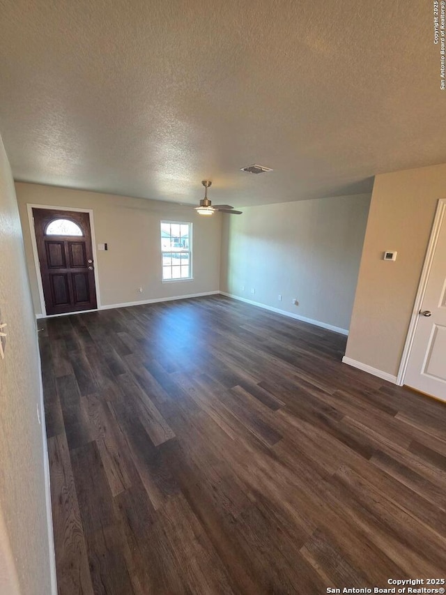 unfurnished living room featuring a ceiling fan, baseboards, visible vents, dark wood-type flooring, and a textured ceiling