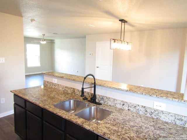 kitchen with a sink, light stone countertops, and dark cabinetry