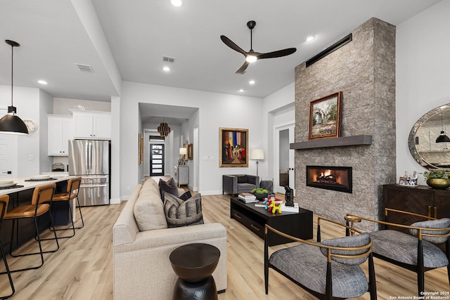 living room with light wood finished floors, visible vents, a fireplace, and a ceiling fan