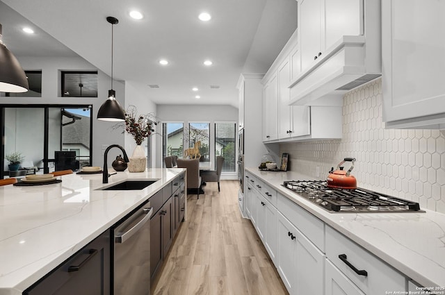 kitchen featuring light wood-style flooring, a sink, stainless steel appliances, white cabinets, and decorative backsplash