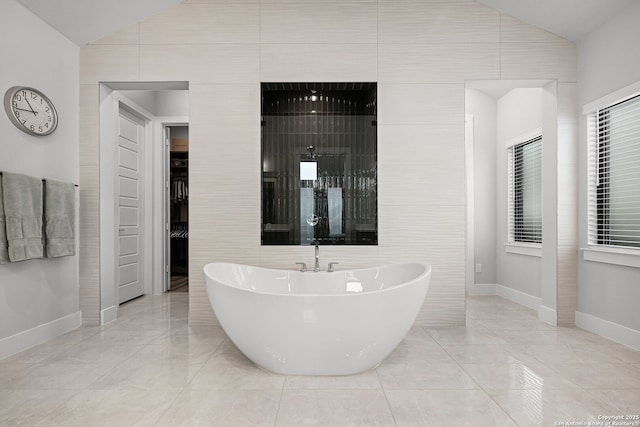 bathroom featuring a spacious closet, a soaking tub, tile walls, and vaulted ceiling