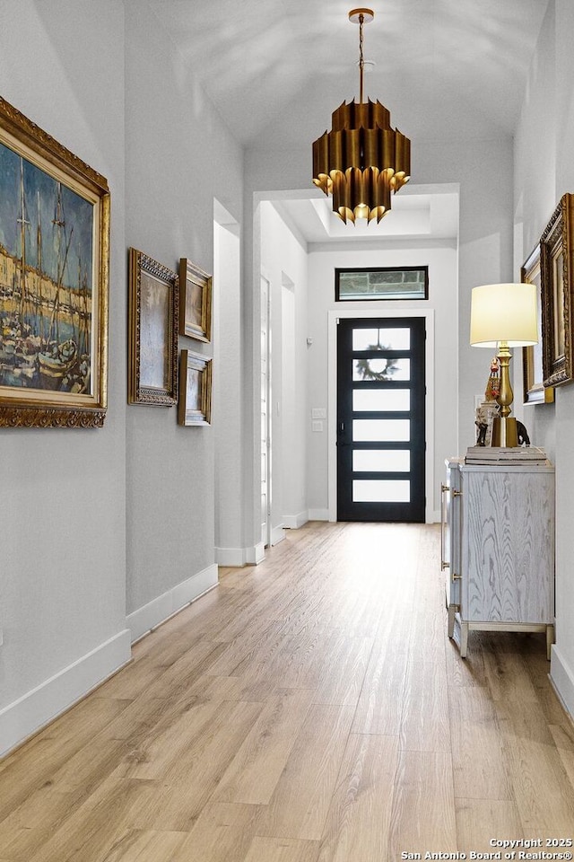 entryway with baseboards, a chandelier, and light wood finished floors