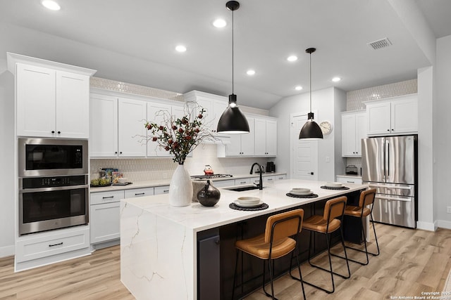 kitchen featuring an island with sink, a sink, white cabinetry, appliances with stainless steel finishes, and light wood finished floors