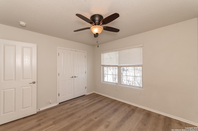 unfurnished bedroom featuring baseboards, wood finished floors, a closet, a textured ceiling, and a ceiling fan