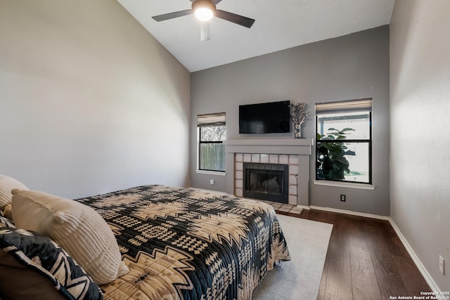 bedroom with ceiling fan, baseboards, a tiled fireplace, vaulted ceiling, and wood finished floors