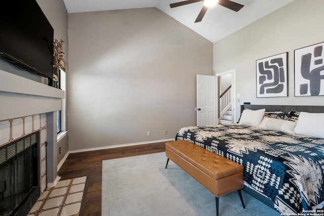 bedroom featuring ceiling fan, baseboards, a tiled fireplace, wood finished floors, and high vaulted ceiling