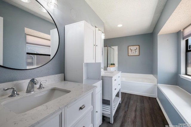 bathroom featuring a garden tub, two vanities, wood finished floors, a textured ceiling, and a sink