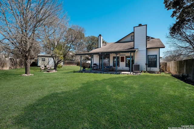 rear view of property featuring central air condition unit, a chimney, a fenced backyard, an outdoor structure, and a ceiling fan