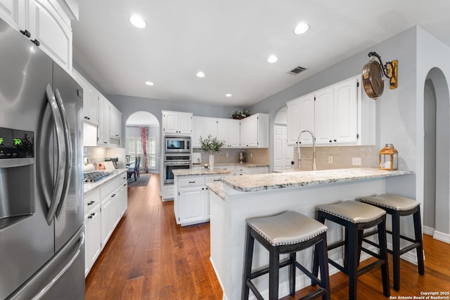 kitchen featuring a peninsula, arched walkways, dark wood-style flooring, stainless steel appliances, and white cabinetry