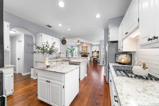 kitchen featuring visible vents, a peninsula, a fireplace, arched walkways, and a sink