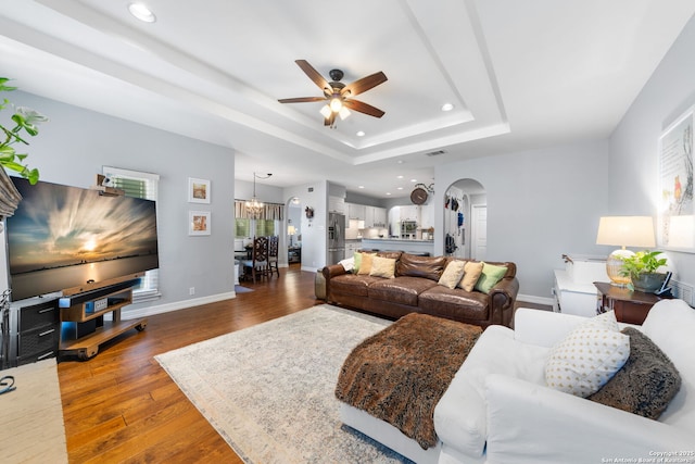 living area featuring a tray ceiling, wood finished floors, recessed lighting, arched walkways, and baseboards