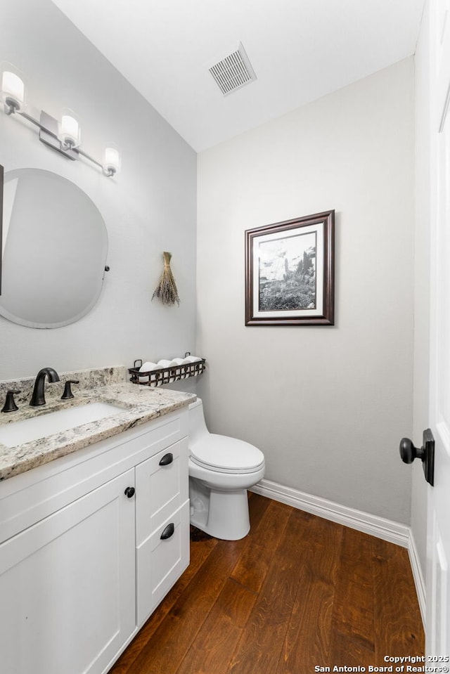 half bath featuring visible vents, baseboards, toilet, wood finished floors, and vanity