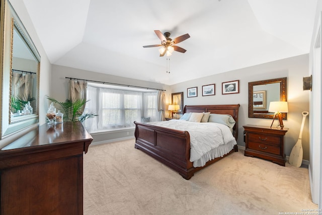 bedroom with baseboards, light carpet, a raised ceiling, and a ceiling fan