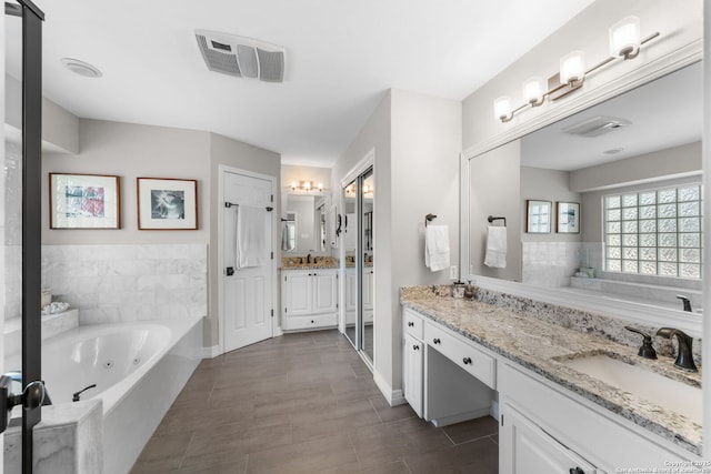 full bathroom featuring two vanities, visible vents, a whirlpool tub, and a sink